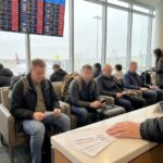Vertrekbord op een luchthaven met vertraagde vluchten en wachtende reizigers ervoor